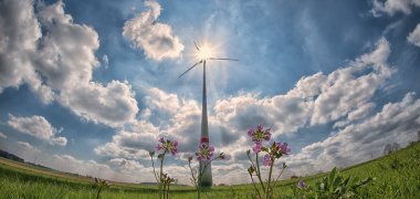 Windrad auf einer grünen Wiese mit Sonne im Hintergrund